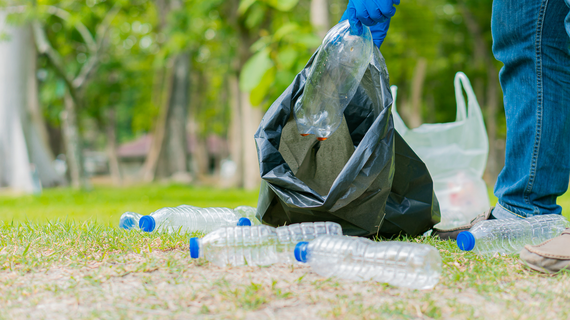 Hand picking plastic bottles on the ground.